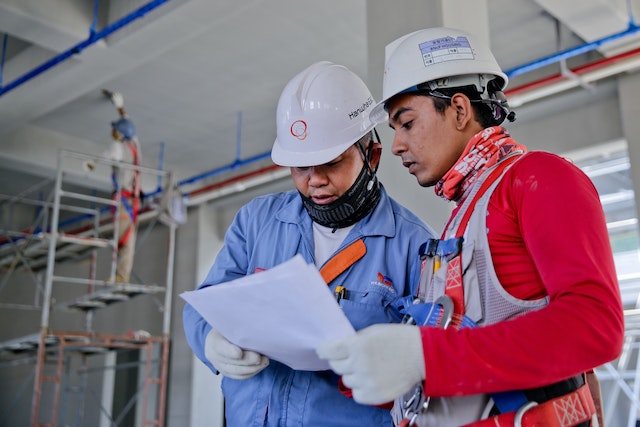 Two men in white hard-hats holding white paper