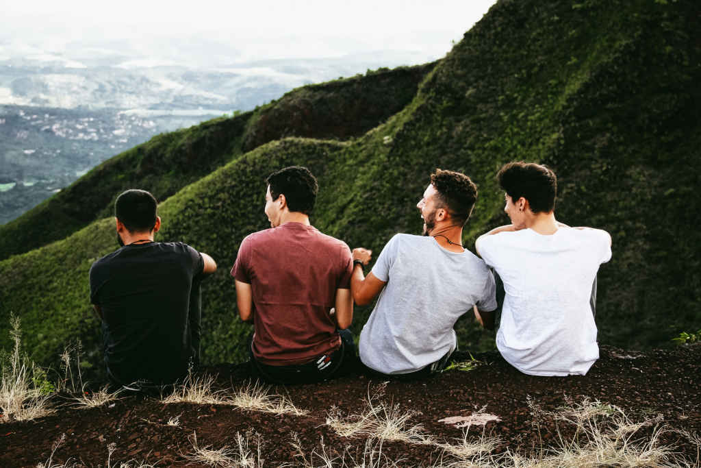 Friends - four men setting on the ground on top of a hill - Photo by Matheus Ferrero on pexels